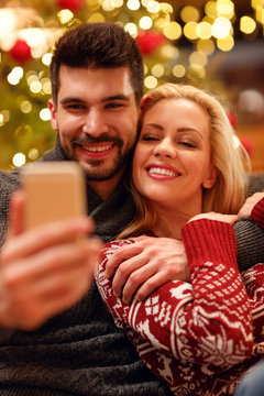 lovely couple in warm sweaters taking selfie picture with smartphone at home.