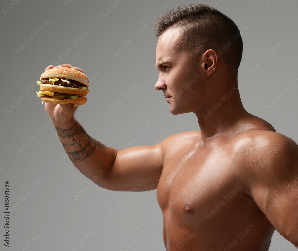 Wall mural Young strong muscular athlete men look at unhealthy junk fast food burger cheeseburger