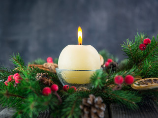 Close up round ivory burning Christmas candle on advent wreath with natural decor on the old rustic table with dark stone background. Christmas festive concept. Selective focus. Space for text