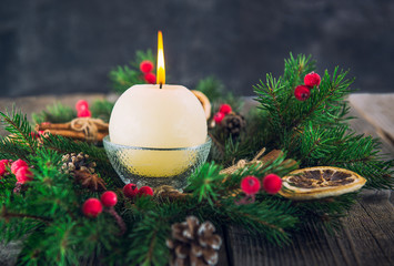 Close up round ivory burning Christmas candle on advent wreath with natural decor on the old rustic table with dark stone background. Christmas festive concept. Selective focus. Space for text