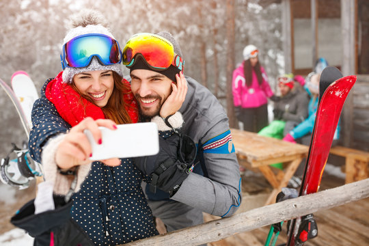 cheerful couple taking selfie together with cell phone in snowy mountain