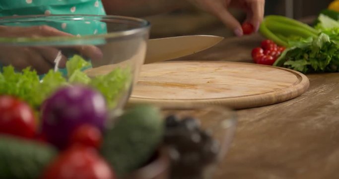 Woman hand prepares salad at home kitchen 4k close-up video. Female cooking side dish: cutting cherry tomatoes with knife, vegetables on table. Healthy food