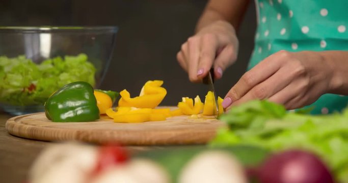 Woman hand prepares salad at home kitchen 4k close-up video. Female cooking side dish: cutting bell pepper with knife, vegetables on table. Healthy food