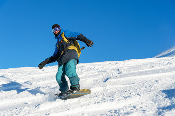 Fototapeta na wymiar Freeride snowboarder rolls on a snow-covered slope leaving behind a snow powder against the blue sky
