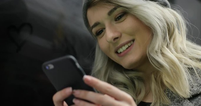 Close-up portrait of a smiling cute girl browsing and typing message on her phone while travelling on the public transport.