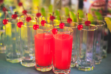 Beautiful line of different coloured cocktails on a party, tequila, martini, vodka, and others on decorated catering bouquet table on open air party, tropic beach hawaiian party setting
