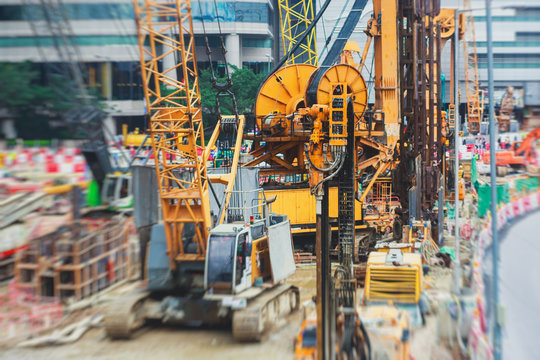 A large construction site in the city, the process of massive buliding construction with heavy vehicle at work, excavator, elevating crane and bulldozer