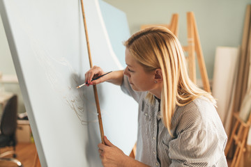 Beautiful blonde woman artist drawing with a brush and pain in her art studio