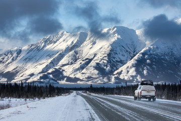 A car driving towards mountains on the Alaska Highway