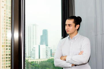 Young business leader concept. Young handsome business man in modern office looking out the window thinking about work