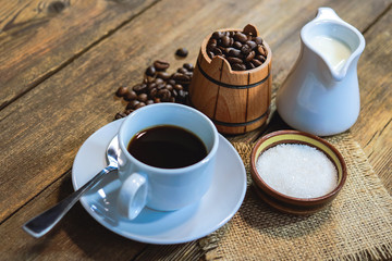 coffee in a white cup. grain coffee in a barrel. a jug of milk. sugar