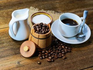 coffee in a white cup. grain coffee in a barrel. a jug of milk. sugar