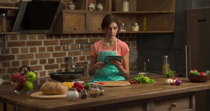 Woman cooking with tablet on home kitchen modern interior 4k video. Female reading preparing recipe and frying omelette or pancakes