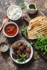 Meatballs, tomato sauce, mozzarella, arugula, grilled bread hot sandwiches ingredients on a wooden table, top view. Delicious snack, breakfast, appetizer