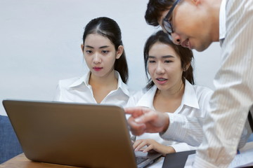 Young Asian business people working together on a laptop computer at office. Teamwork brainstroming concept. Selective focus and shallow depth of field.