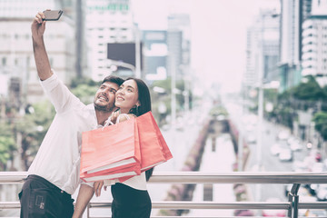 Happy couple taking selfie with mobile phone after a hard day of huge sale shopping in asian country.