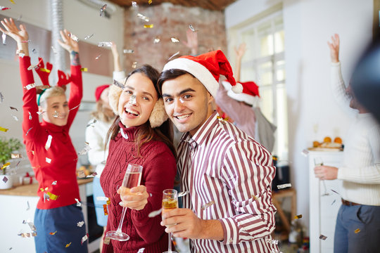 Young cheerful couple with champagne wishing you merry Christmas while enjoying party