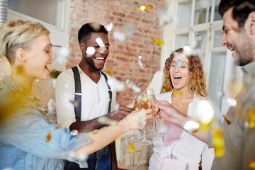 Ecstatic girls and their boyfriends clinking with champagne flutes in confetti fall