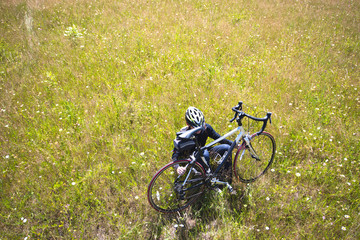 Cyclist resting from trip while sitting in meadow with grass and field flowers holding her bicycle