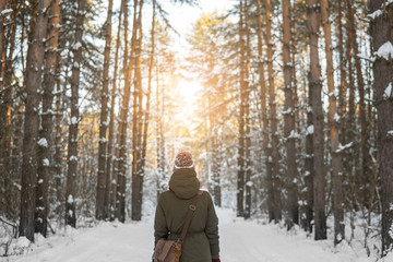 Woman walks a winter forest with the morning light streaming through the trees and illuminating the pine trees behind.