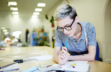 Young dress designer looking at her sketch and thinking of some curious details
