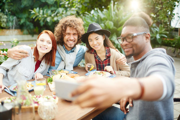 Young affectionate friends making selfie after or during dinner in garden room