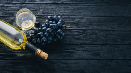 A bottle of wine with glasses and grapes on a black wooden background. Free space for text. Top view.