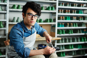 Young serious cobbler with pliers and workpiece doing his work in workshop