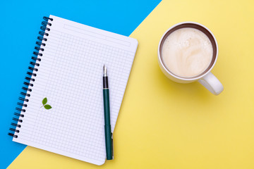 Top view on blank notebook with pen and cup of coffee, separated on yellow and blue paper background.