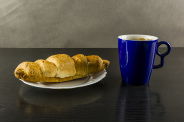 Gold croissant and a cup of coffee for breakfast.