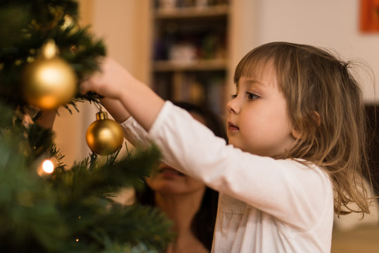 Little girl hanging christmas ball on a tree