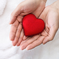 Obraz premium Man holding red heart in his hands. Textile heart in male hands on a light soft background.