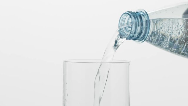 Slow motion pouring mineral water into glass from plastic bottle over white background