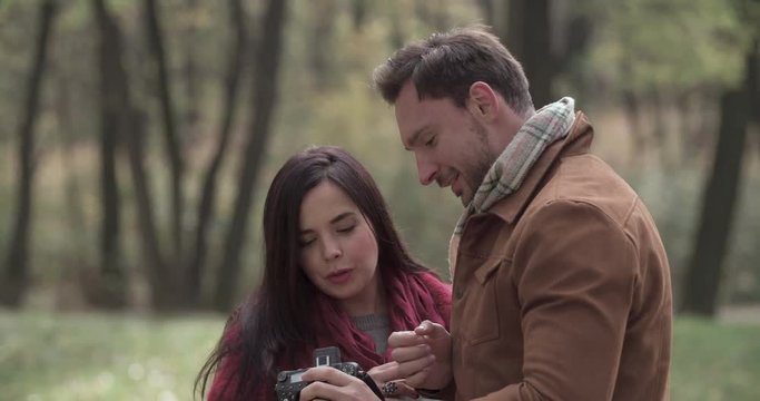 Loving couple photographing in autumn forest park 4k date video. Young man and overweight fat woman looking photo shoots on digital camera. Love story romance concept