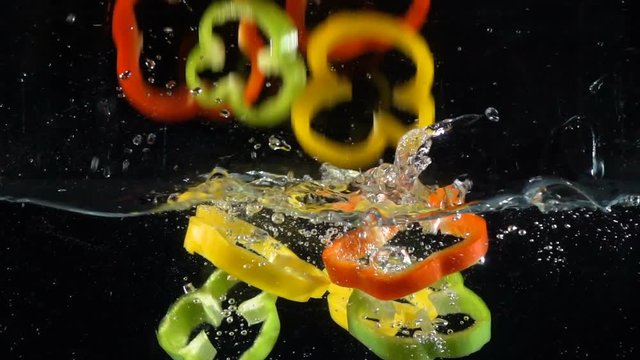 Colorful paprika rings falling in water on black background