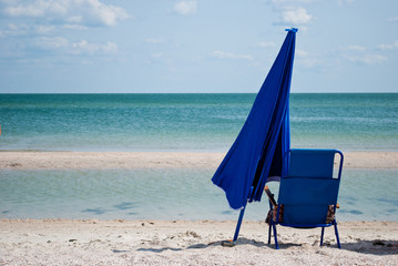 Blue beach chair and blue big closed umbrella for shade on the shore of the blue sea Island of sand in the water blue sky white clouds sea wave beautiful landscape summer vacation beach sand weekend r