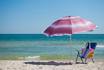 Blue beach chair and pink bag and pink big open umbrella for shade on the shore of the blue sea Island of sand in the water blue sky sea wave beautiful landscape summer vacation beach sand weekend