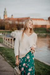 Beautiful young blonde walking along the embankment near river and posing at sunset in summer