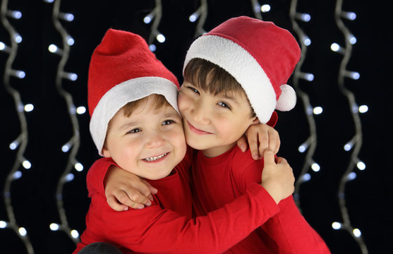 niños felices sonriendo disfrazados de santa claus dándose un abrazo en un fondo negro con luces blancas