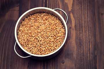 uncooked spelt in pot on wooden background