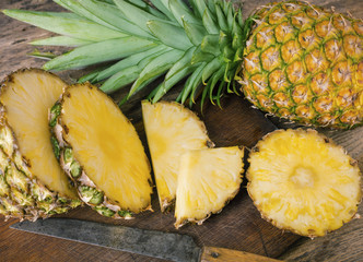 Pieces and whole pineapple with knife on kitchen board