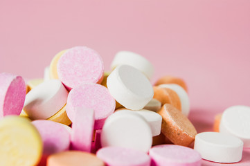 Close up of pile of chewable antacid acid indigestion relief tablets with fruit flavour in pastel colors, such as pink, yellow, orange and white on light pastel pink background