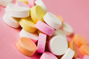 Close up of pile of chewable antacid acid indigestion relief tablets with fruit flavour in pastel colors, such as pink, yellow, orange and white on light pastel pink background