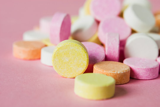 Close up of pile of chewable antacid acid indigestion relief tablets with fruit flavour in pastel colors, such as pink, yellow, orange and white on light pastel pink background