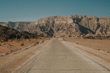 Timna National Park in Israel. Long asphalt road and rocky hill on desert in Israel with blue sky in background.