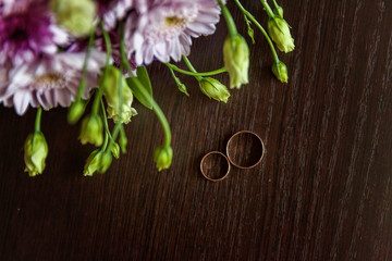 Beautiful wedding rings lie on a table against the background of a bouquet of flowers