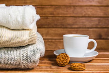 Stack of cozy knitted warm sweater , wooden background . Sweaters in retro Style and a Cup of hot drink. The concept of warmth and comfort.