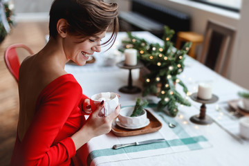 Beautiful young woman in a red dress is covering the table for the christmas evening