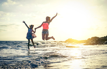 Fototapeta premium Szczęśliwa kochająca rodzina matki i córki, skoki w wodzie o zachodzie słońca na plaży - mama z dzieckiem, wspólna zabawa w letni dzień - koncepcja lato, podróże, wakacje i rodzina