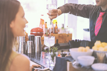 Young woman waiting her drink at bar counter - Professional bartender serving a cocktail to people...